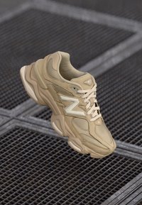 Baskets New Balance beiges avec un design en couches. Comprend des matériaux en maille et en daim, un logo "N" bien visible et une semelle rembourrée.