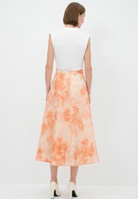 Langer, fließender Rock aus weichem, leichtem Stoff mit einem orangefarbenen Blumenmuster, kombiniert mit einem figurbetonten weißen Oberteil und creamfarbenen High Heels.
