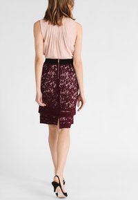 Burgundy spetsskjorta med en elastisk midja och slits bak. Komplett med en ljusbeige veckad topp och svarta högklackade skor.