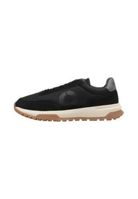Zapatillas deportivas negras con un upper texturizado, que presentan un logo negro, una entresuela color crema y una suela exterior de goma para mayor tracción.