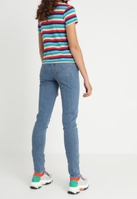 Camisa de manga corta a rayas en verde, azul, rojo y blanco; pantalones vaqueros ajustados azules; deportivas blancas con acentos coloridos.