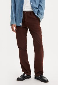 Pantaloni din bumbac maro cu croială dreaptă, buzunare laterale și închidere cu nasture, asortați cu o cămașă din denim și mocasini negri.