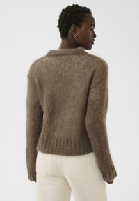 Pull en maille marron et duveteuse avec un ourlet et des poignets côtelés. Présente un col rond et une coupe décontractée. Le tissu texturé apporte de la profondeur.