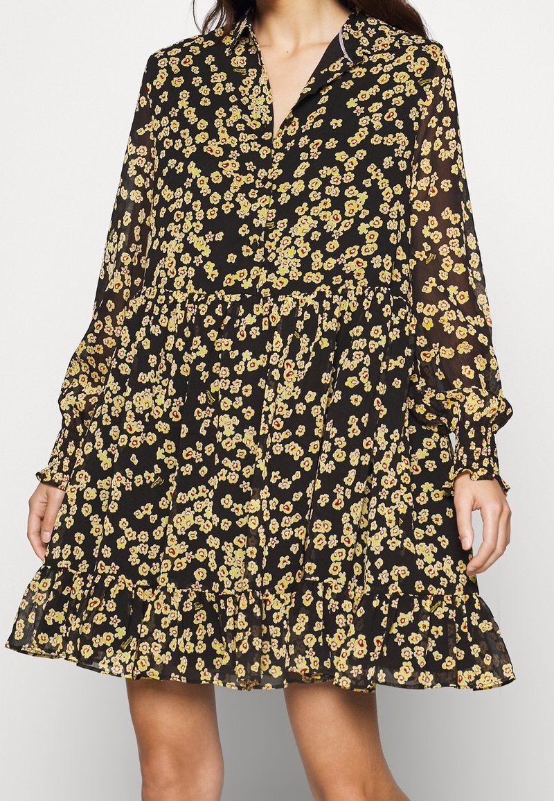 Abito nero con un motivo floreale che presenta piccoli fiori gialli e rossi, design con bottoni, maniche lunghe e un orlo arricciato.