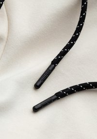 Cordon de sweat à capuche tacheté noir et blanc avec embouts en plastique noir embossés "OMBRE" sur fond en tissu crème.