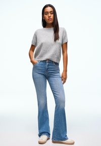 Pull gris en maille à manches courtes associé à un jean évasé bleu clair et des baskets crème, avec une coupe décontractée et une texture lisse.