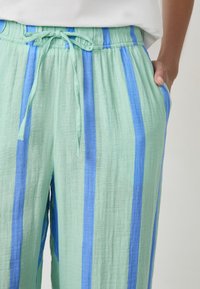 Pantaloni leggeri verdi con strisce blu, dotati di vita elastica, cordino di regolazione e tasche laterali. Tessuto testurizzato con una vestibilità rilassata.