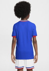 Jersey de manga corta azul con acentos rojos y blancos, tela texturizada, cuello redondo, acompañado de pantalones cortos blancos con rayas rojas y azules.
