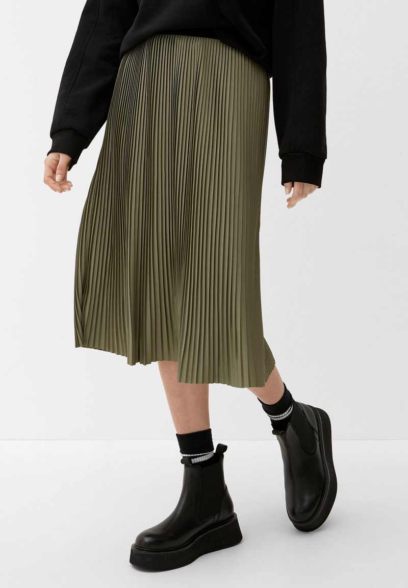 Falda midi de color verde oliva con pliegues, hecha de una tela ligera; combinada con botas de plataforma negras y calcetines elásticos con rayas blancas.
