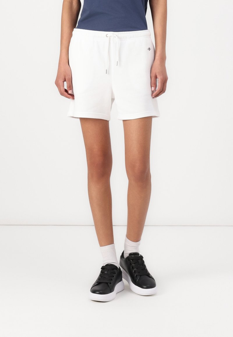 Witte katoenen shorts met een elastische tailleband en trekkoord, met een klein logo aan de linkerkant. Gecombineerd met zwarte sneakers.