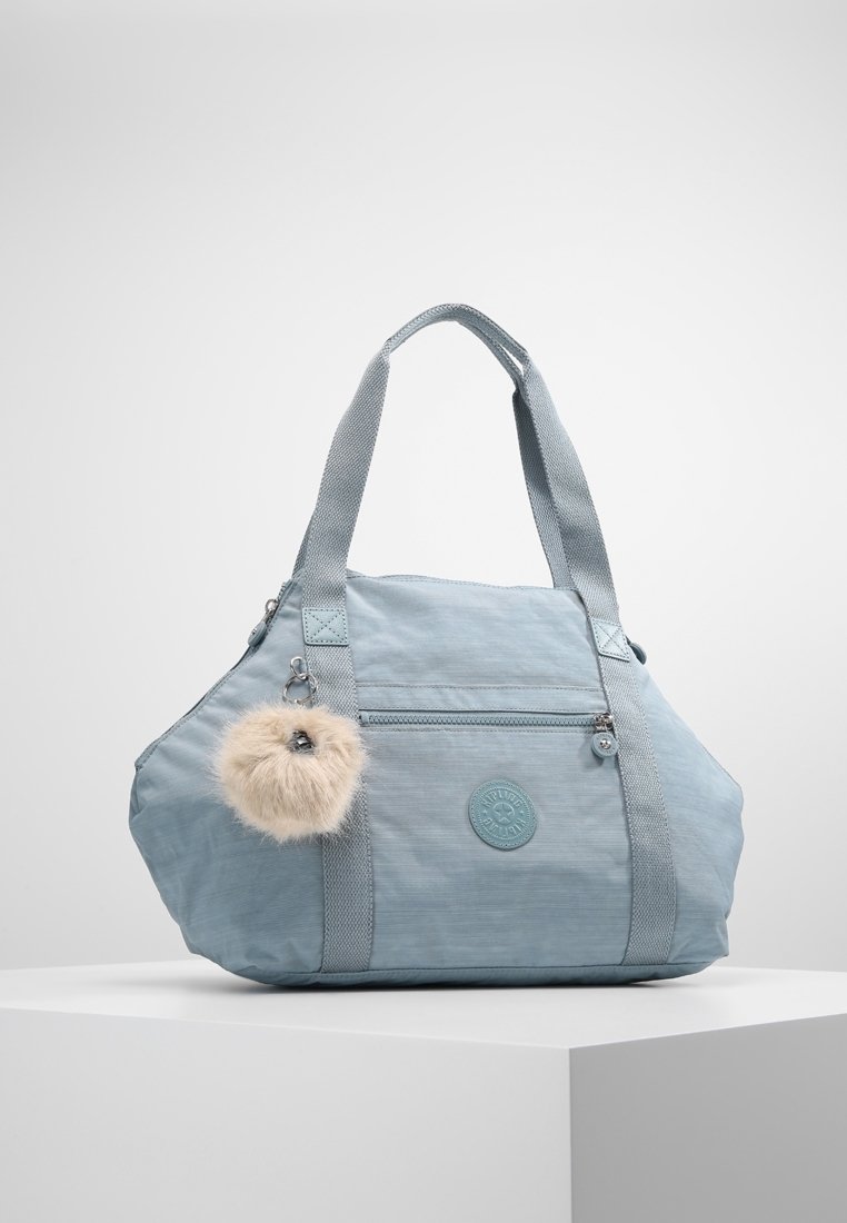 Sac cabas bleu clair en tissu texturé, avec deux anses supérieures, une fermeture éclair et un accessoire pompon en fausse fourrure attaché.