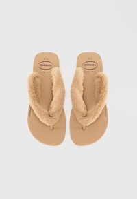 Brune flip-flop med myk faux fur-stropp og teksturert fotseng, med et minimalistisk design og en subtil logo på fotsengen.