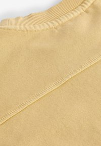 Primer plano de una tela de punto amarillo pálido que muestra el cuello acanalado y los detalles de la costura diagonal.