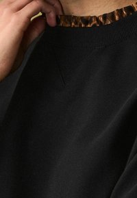 Sweat-shirt noir avec un col texturé et côtelé orné d'un imprimé léopard. Le détail inclut une couture en forme de V au niveau du col.