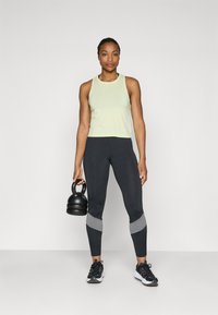 Light green athletic tank top, black leggings with gray accents, and black sneakers. Person holding a black kettlebell.