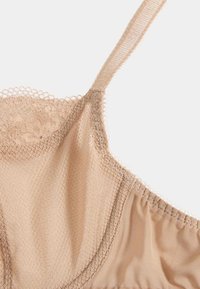 Beige undertøjstop med blonder langs halsudskæringen og justerbare spaghetti-stropper; blødt, let meshstof.