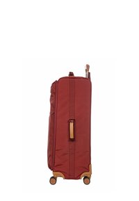 Valise en tissu rouge au design robuste, avec des accents marron et une poignée rétractable. Équipée de quatre roues et d'une poignée de transport sur le côté.