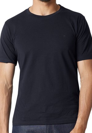 Mann trägt ein schlichtes schwarzes T-Shirt mit kurzen Ärmeln und blauen Jeans, beschnitten am Hals und in der Mitte des Oberschenkels.