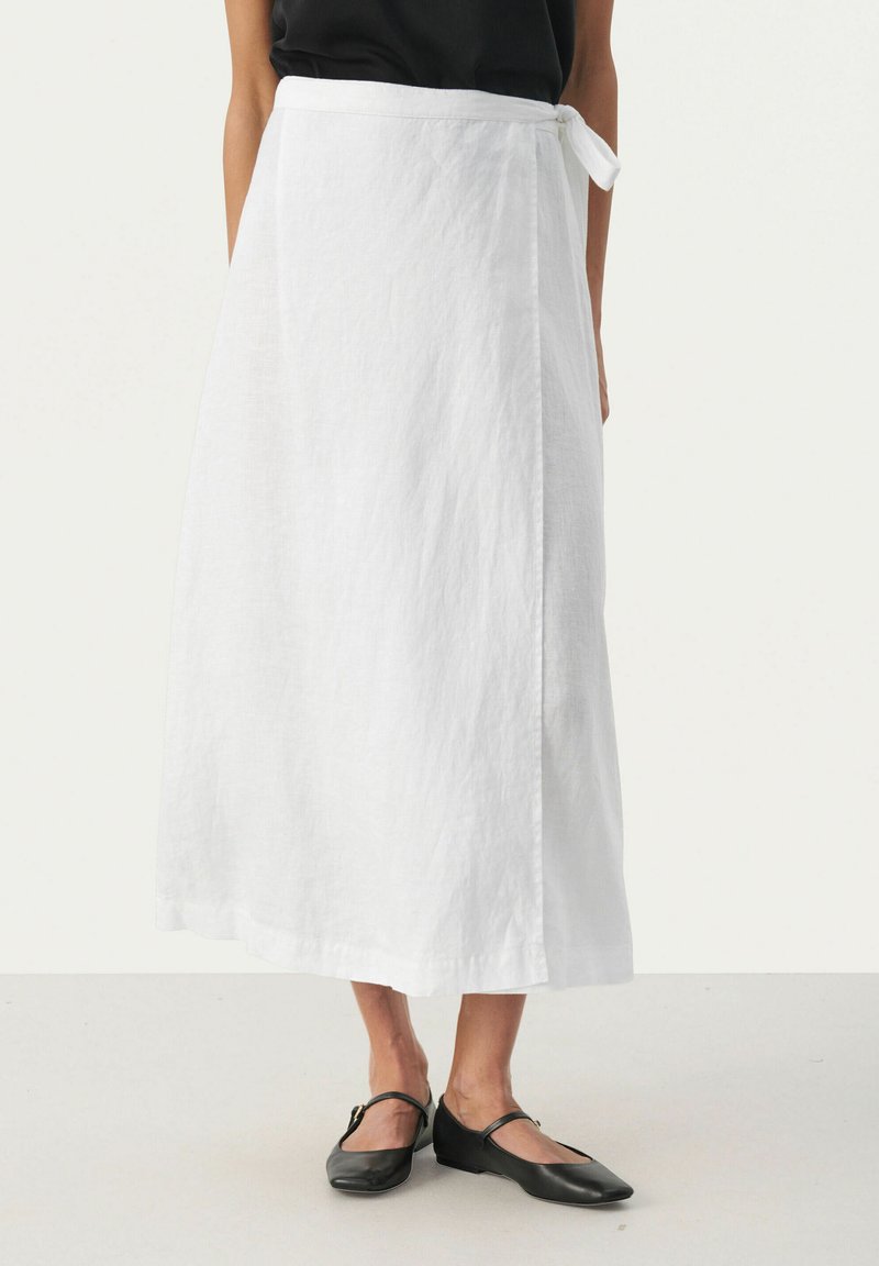 White linen wrap skirt with a tied waist, featuring a flowing design and a smooth texture. Paired with black flat shoes.