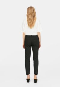Czarne dopasowane spodnie z nogawkami slim fit, z kantem z przodu, dwoma tylnymi kieszeniami, noszone z luźną białą koszulką i czarnymi butami na obcasie.