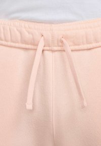 Pantalones de chándal rosa claro con una textura suave, que presentan un cordón en la cintura elástica y un acabado de tela lisa.