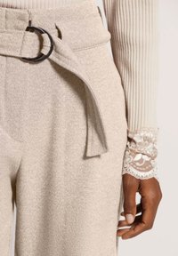 Beige, textuur hoge taille broeken met een stoffen riemlus en een donkere ronde gesp, gecombineerd met een ribbelige lichte top met kantaccenten.
