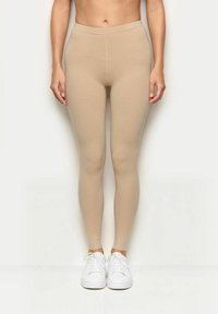 Leggings beige con una vestibilità aderente, realizzati in materiale elastico, con una superficie liscia e una vita alta, abbinati a sneaker bianche.