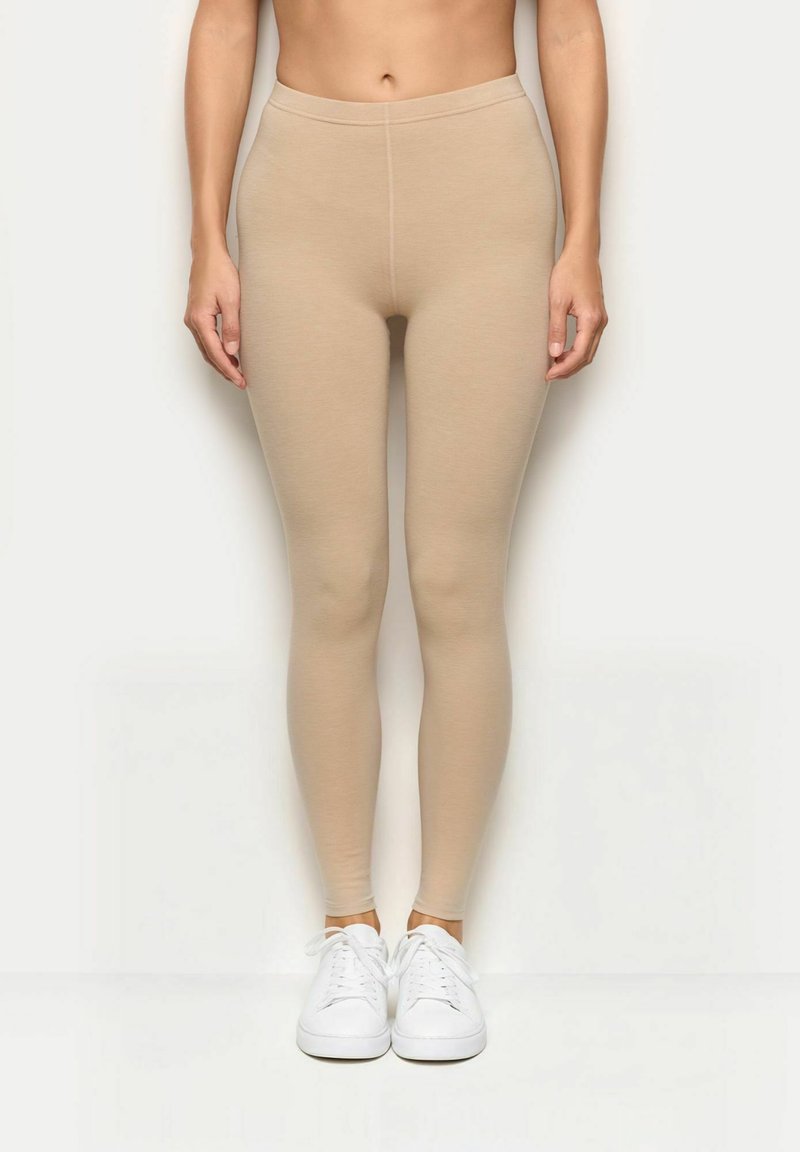 Leggings beige con una vestibilità aderente, realizzati in materiale elastico, con una superficie liscia e una vita alta, abbinati a sneaker bianche.