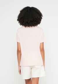 Világos rózsaszín pamut póló rövid ujjal, kerek nyakkal és laza szabással. A modellen fehér rövidnadrággal viselve, sima hátulnézettel.