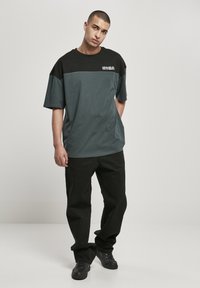 Kortsleeve t-skjorte, svart og teal fargeblokkdesign, laget av bomull, løs passform. Svart bukser og sko fullfører antrekket.