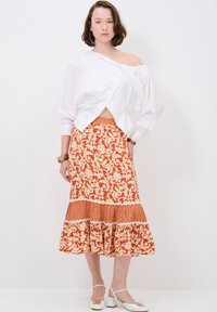 Blouse blanche à épaules dénudées associée à une jupe orange à motifs floraux en couches avec un ourlet froncé et des accents de vichy. Chaussures à talons bloc blanches.