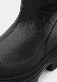 Botte en cuir noir texturé avec panneau latéral élastique et semelle épaisse en caoutchouc, mettant en avant les détails de l'avant supérieur et de la semelle.