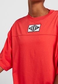 Röd t-shirt i bomull med korta ärmar, utrustad med en rektangulär svartvit logotypmärke vid halsringningen och en avslappnad passform.