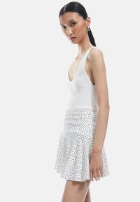 Top bianco a righe abbinato a una gonna bianca svasata con pois neri. L'outfit presenta un design casual e aderente con una texture morbida.