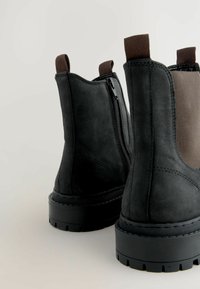 Mustadest pehmetest nahast ankle saapad, millel on elastsed küljed, tõmblukk ja paks kummitald, millel on tekstuuripind ja tugevdatud õmblused.