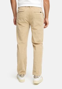Beige corduroy trousers with a straight-leg fit, featuring two back pockets, subtle texture, and worn with white sneakers.