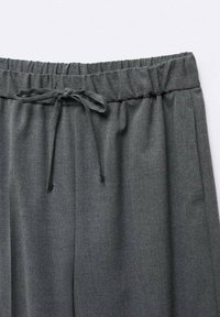 Pantalon gris foncé avec taille élastique et cordon noué, avec poches latérales et texture de tissu lisse.