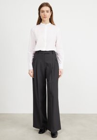 Camicia bianca con colletto alla coreana, abbinata a pantaloni neri a vita alta con gamba larga, indossata con scarpe nere. Design semplice.