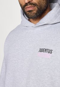 Hallhallane kapuutsiga pusake, mis on valmistatud pehmest kangast. Rinnal on must ja roosa tekst "JUVENTUS MILLE897". Tavaline lõige, juhuslik disain.