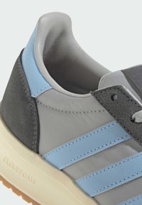 Šedá a černá sportovní bota se světle modrými akcenty a strukturovanými materiály. Má zakřivený límec a nápis "CLOUDfoam" na podrážce.