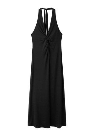 Femme aux cheveux bruns courts portant une robe noire dos nu à col halter et des sandales noires, debout devant un fond clair uni.