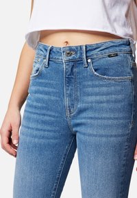 Vaqueros de denim azul de cintura alta con una textura suave, ligero desgaste, cinco bolsillos y cierre de botón metálico.