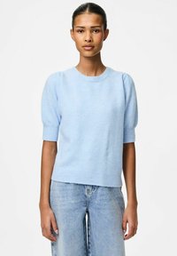 Ljusblå kortärmad stickad tröja med rund halsringning, ribbade ärmslut och avslappnad passform, i kombination med ljusblå denimjeans.