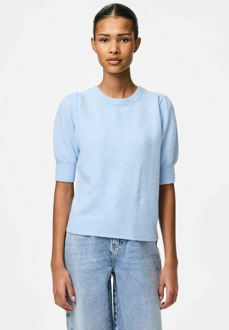 Ljusblå kortärmad stickad tröja med rund halsringning, ribbade ärmslut och avslappnad passform, i kombination med ljusblå denimjeans.