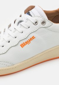 Baskets en cuir blanc avec le logo orange "Blauer", lacets blancs, œillets en argent, et une semelle texturée beige avec un accent orange.