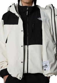 White and black jacket featuring a hood, zip front, and fleece lining. Includes snap buttons and a labeled tag on the sleeve.