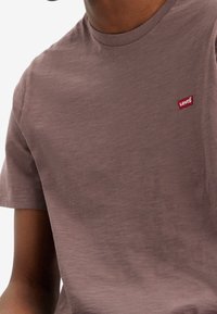 Brun kortärmad T-shirt med rundad hals, tillverkad av lätt material. Har en liten röd Levi's-logotyp på bröstet.
