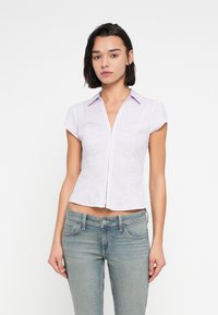 Κοντομάνικο, εφαρμοστό πουκάμισο σε ανοιχτό μωβ χρώμα με καρό σχέδιο, διαθέτει γιακά και εμπρόσθιο φερμουάρ. Φοριέται με τζιν ανοιχτού χρώματος.