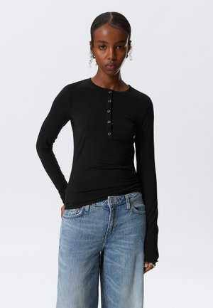 Black long-sleeve shirt with a round neckline and five button placket, paired with light blue wide-leg jeans. Smooth texture.