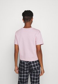 Rosa bomullströja med korta ärmar, rund halsringning och cropped passform, tillsammans med svart och vit rutig byxor.